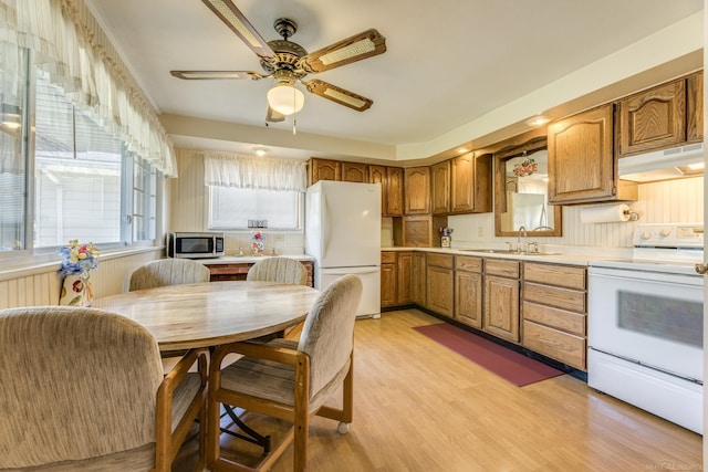 kitchen featuring white appliances, under cabinet range hood, light countertops, a sink, and brown cabinets