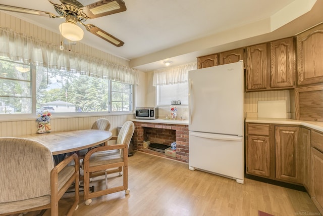 kitchen featuring stainless steel microwave, light countertops, freestanding refrigerator, brown cabinetry, and light wood finished floors