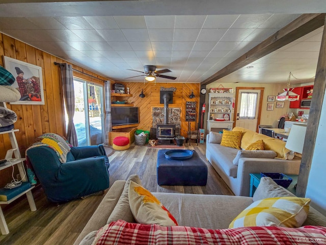 living area with wood finished floors, wooden walls, a ceiling fan, and a wood stove