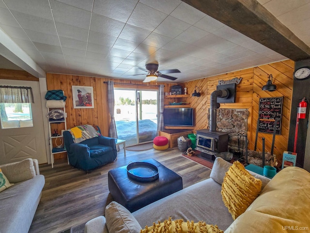 living area featuring wood finished floors, wood walls, ceiling fan, and a wood stove
