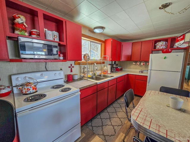 kitchen featuring white appliances, a sink, red cabinetry, and wood finished floors