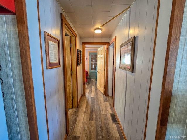 hallway with dark wood-style flooring, wood walls, and visible vents