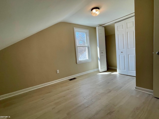 additional living space with light wood-style floors, baseboards, lofted ceiling, and visible vents