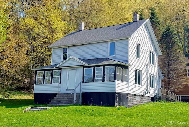 traditional-style house featuring entry steps, a front lawn, a shingled roof, and a wooded view