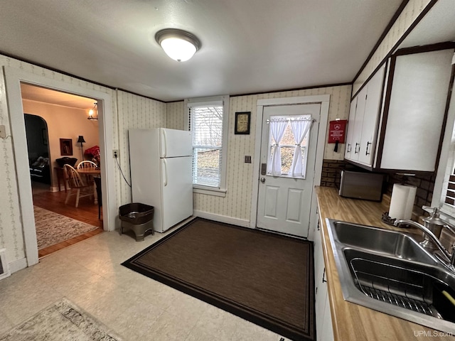 kitchen featuring wallpapered walls, tile patterned floors, a sink, and freestanding refrigerator