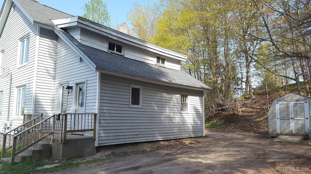 view of side of home with roof with shingles, an outdoor structure, a chimney, and a storage unit