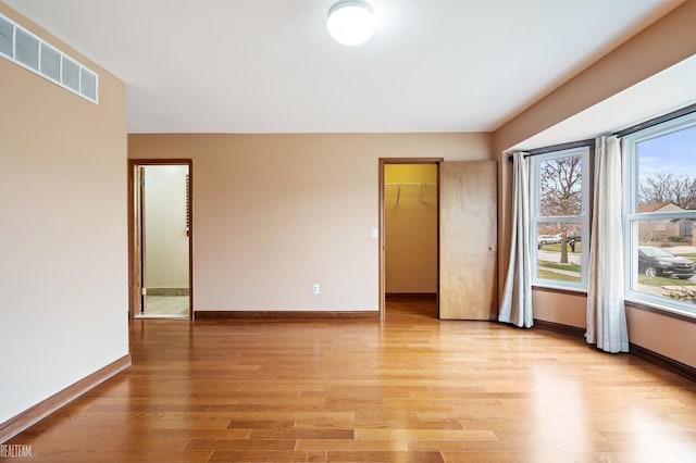 empty room with light wood finished floors, visible vents, and baseboards