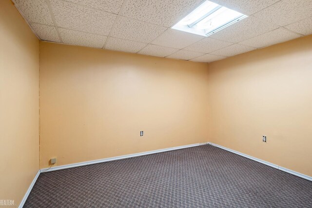 spare room featuring carpet, baseboards, and a drop ceiling