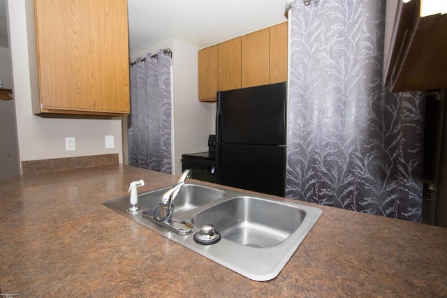 kitchen featuring a sink, freestanding refrigerator, and dark countertops