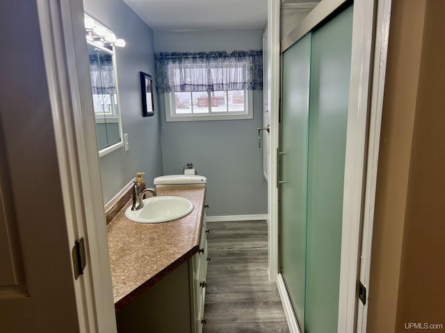 full bathroom with wood finished floors, double vanity, a sink, and a shower with door