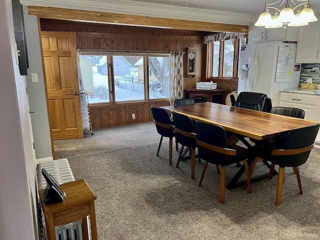 carpeted dining room with wood walls, a notable chandelier, and ornamental molding