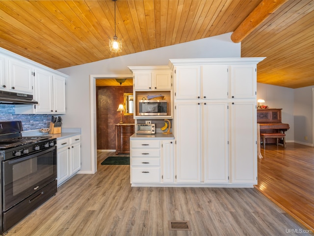 kitchen with stainless steel microwave, under cabinet range hood, gas stove, and lofted ceiling