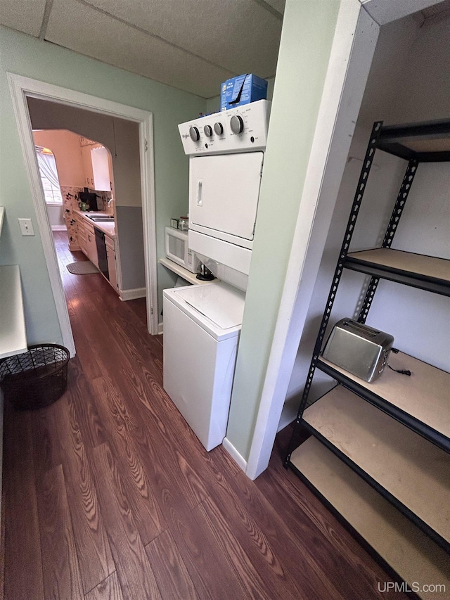 laundry room featuring dark wood-style floors, stacked washer and dryer, and baseboards