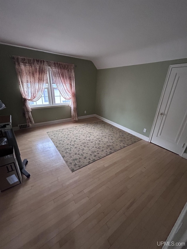 unfurnished living room featuring wood finished floors, baseboards, and vaulted ceiling