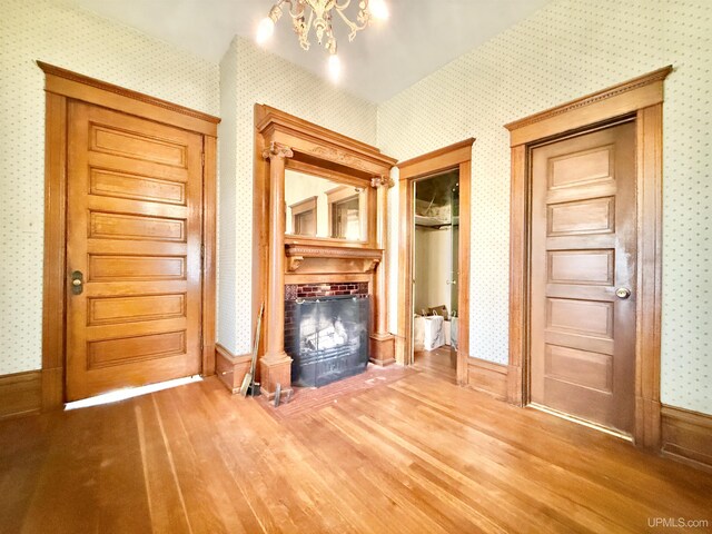 404 Lake Shore Dr, Escanaba, MI 49829 - unfurnished living room featuring wallpapered walls, a fireplace, wood finished floors, a chandelier, and baseboards