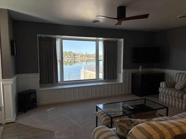 living room featuring a wood stove, visible vents, ceiling fan, and wainscoting