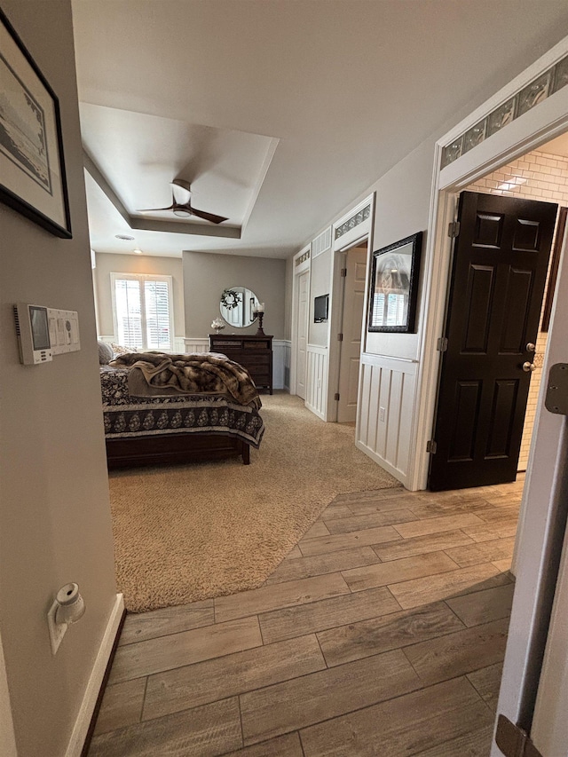 bedroom with a tray ceiling, ceiling fan, wainscoting, and wood finished floors