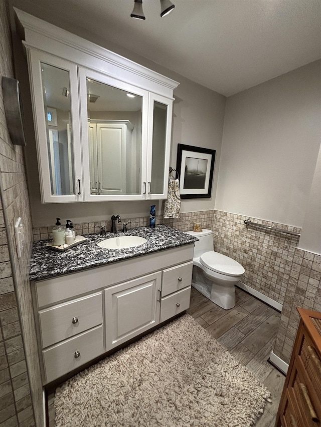 bathroom with vanity, toilet, a wainscoted wall, tile walls, and wood finished floors
