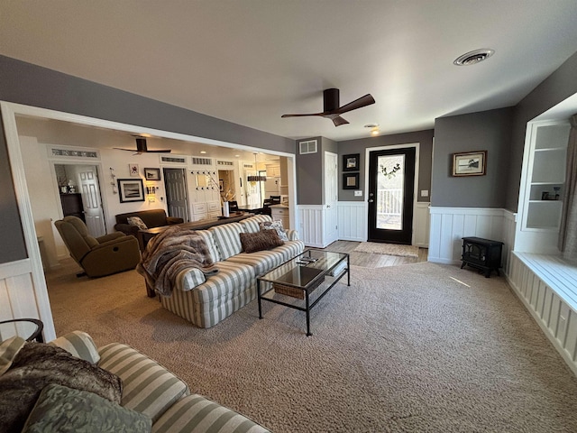 living area featuring visible vents, a wainscoted wall, and ceiling fan