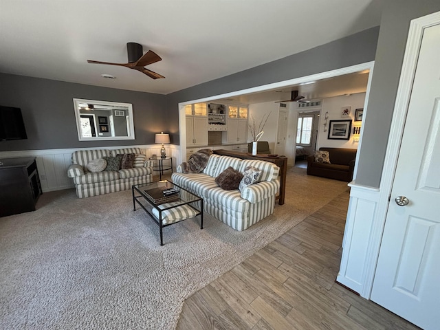 living room featuring wood finished floors, a ceiling fan, and a wainscoted wall