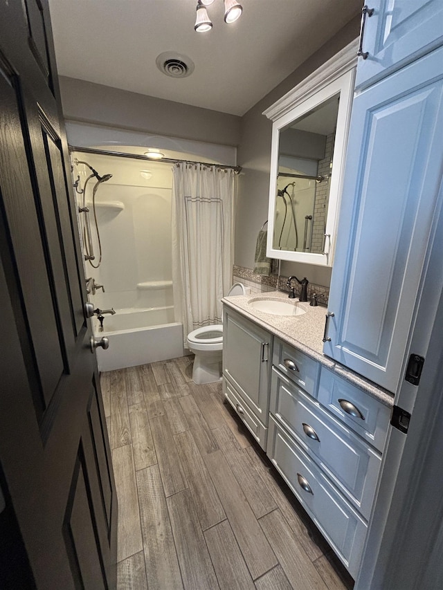 bathroom with vanity, visible vents, toilet, wood finished floors, and shower / tub combo
