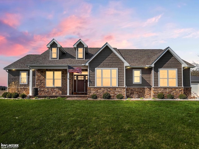 craftsman house with a front yard, roof with shingles, and stone siding