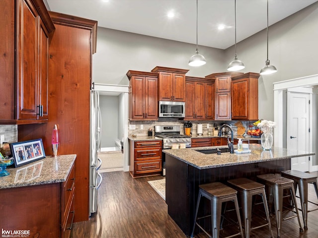 kitchen featuring a kitchen breakfast bar, dark wood-style flooring, a sink, stainless steel appliances, and backsplash
