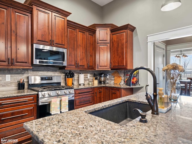 kitchen featuring tasteful backsplash, appliances with stainless steel finishes, a sink, and light stone countertops