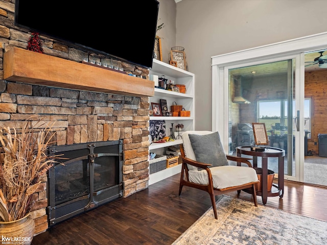 sitting room with wood finished floors, ceiling fan, and a stone fireplace