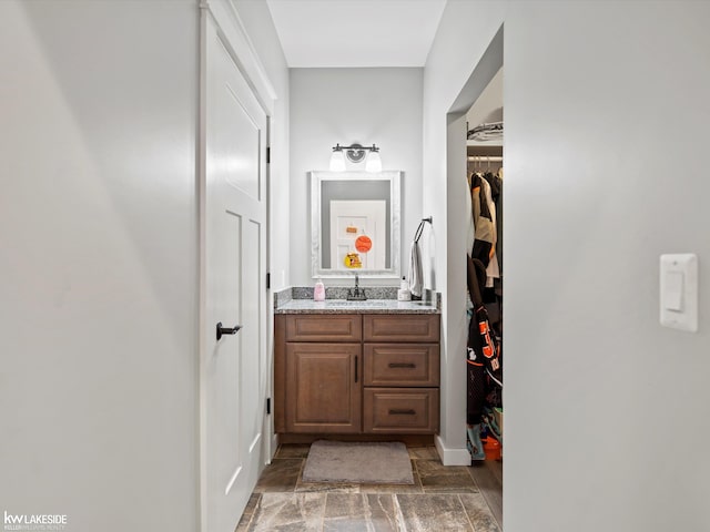 bathroom with stone tile flooring, a spacious closet, vanity, and baseboards