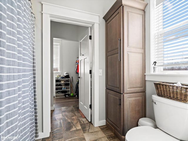 full bathroom featuring toilet, baseboards, and stone finish flooring