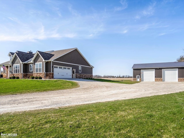 view of front of property featuring a front yard, driveway, stone siding, and a detached garage