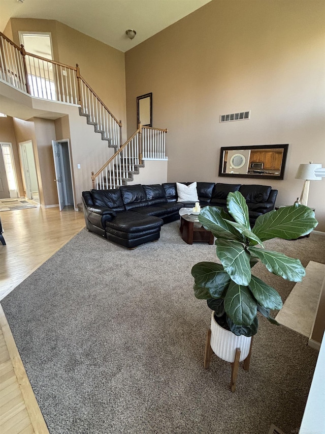 living area featuring a towering ceiling, wood finished floors, visible vents, and stairs