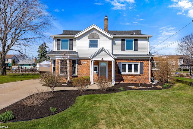 traditional-style house with a chimney, driveway, a front yard, and brick siding