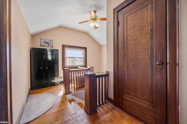interior space with lofted ceiling, baseboard heating, a textured ceiling, ceiling fan, and wood-type flooring