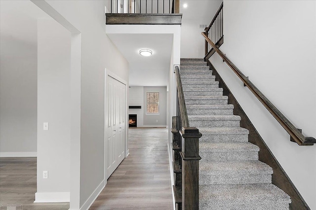 stairway featuring wood finished floors, baseboards, and a warm lit fireplace