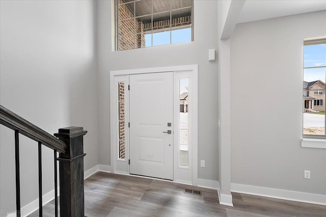 entryway with a towering ceiling, visible vents, baseboards, and wood finished floors