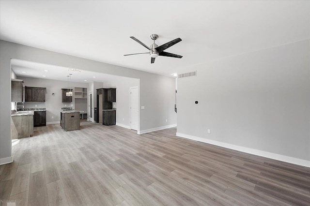 unfurnished living room with light wood-style floors, ceiling fan, visible vents, a sink, and baseboards