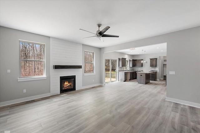 unfurnished living room featuring light wood-style flooring, ceiling fan, baseboards, and a fireplace