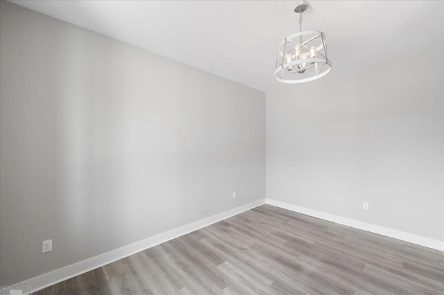 empty room with baseboards, a notable chandelier, and wood finished floors