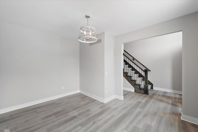 empty room featuring visible vents, baseboards, an inviting chandelier, stairway, and wood finished floors
