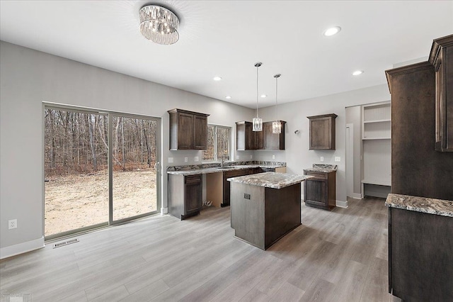 kitchen featuring light wood-type flooring, baseboards, dark brown cabinets, a kitchen island, and visible vents