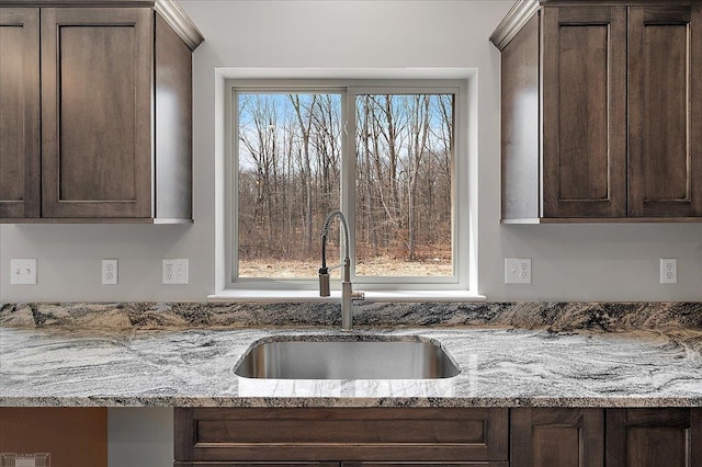 kitchen with light stone counters, a sink, and dark brown cabinets