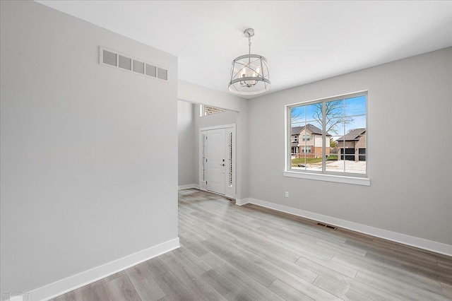 spare room with visible vents, baseboards, a notable chandelier, and wood finished floors