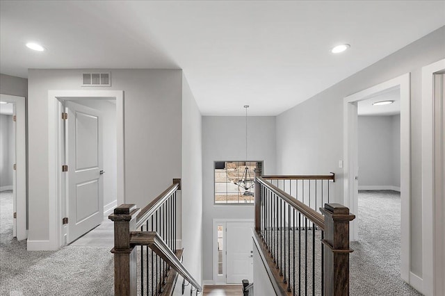 hall with visible vents, an upstairs landing, an inviting chandelier, and carpet