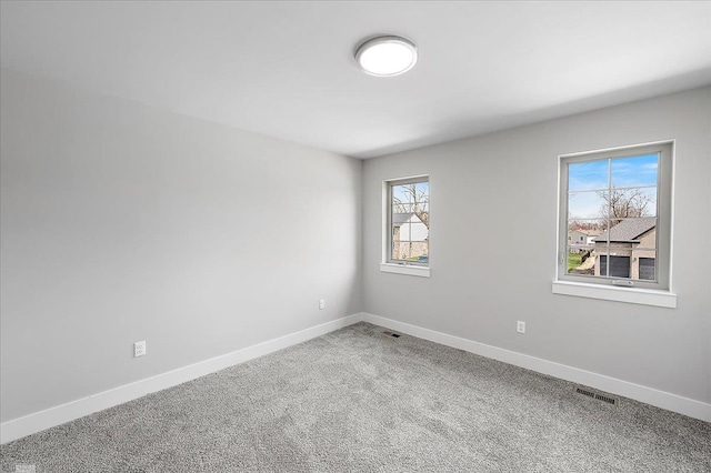 carpeted spare room with visible vents, baseboards, and plenty of natural light