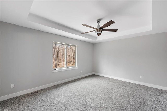 carpeted empty room featuring a tray ceiling, baseboards, a ceiling fan, and visible vents