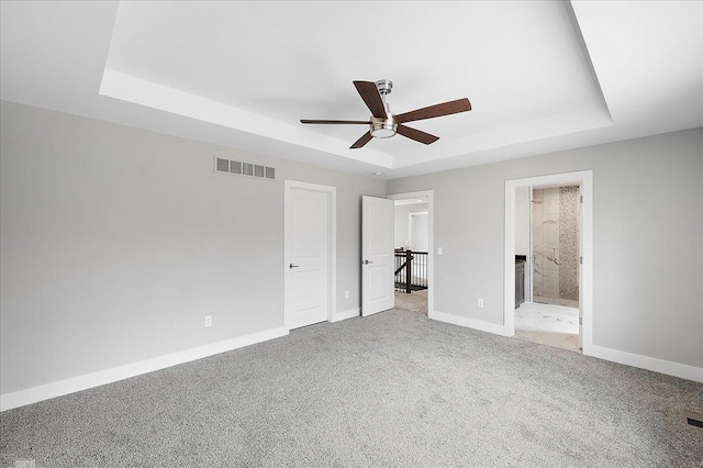unfurnished bedroom featuring carpet, a tray ceiling, a ceiling fan, visible vents, and baseboards