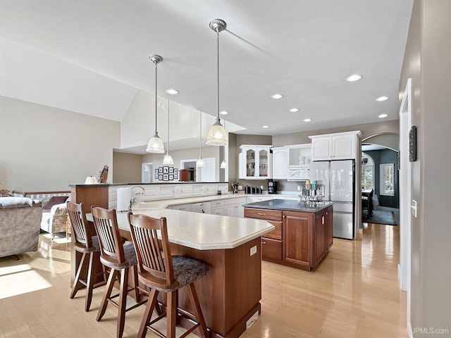 kitchen with light wood-type flooring, freestanding refrigerator, white cabinetry, and arched walkways