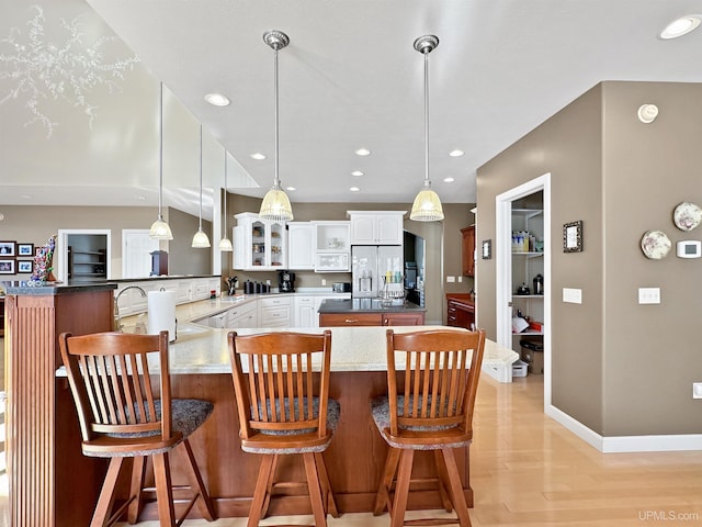 kitchen featuring glass insert cabinets, a kitchen bar, a peninsula, light wood-type flooring, and stainless steel refrigerator with ice dispenser